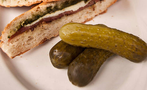 small pickles on a plate next to a sandwich