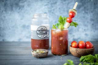 Bloody Mary cocktail with ingredients and McClure's bottle on a wooden surface