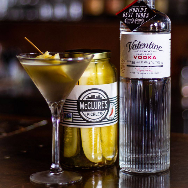 Bottle of Valentine vodka, jar of McClure's pickles, and cocktail with a pickle skewer on a bar.