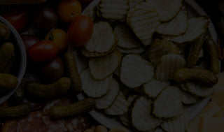 Assorted pickled vegetables including sliced cucumbers, tomatoes, and gherkins on a white plate.