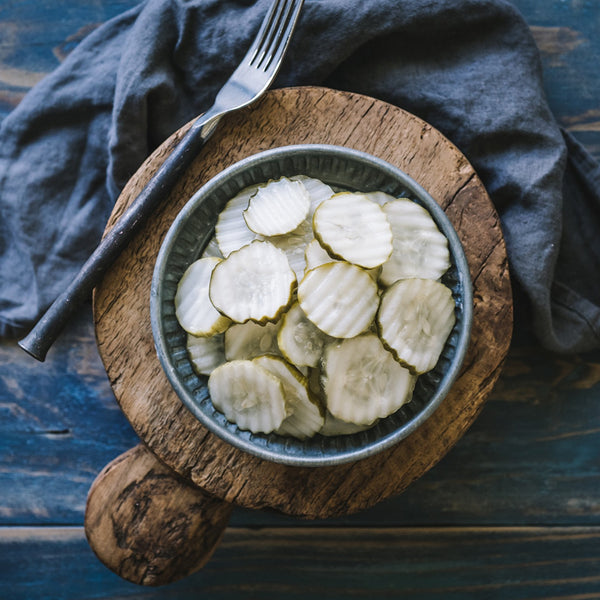Sliced McClure's pickles in a metal bowl on a wooden board with a blue cloth background