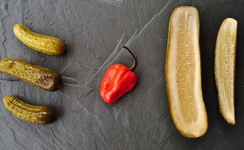 pickles on a slate board with a hot pepper